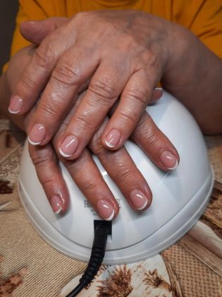 Маникюр с гель-лаком: аккуратные ногти с френчем под УФ-лампой на столе.