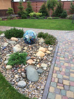 Небольшой каменный садик с декоративным фонтаном (мозаичный шар) напротив лавочки для отдыха. В темное время суток фонтан подсвечивается светильником, вмонтированным в землю 