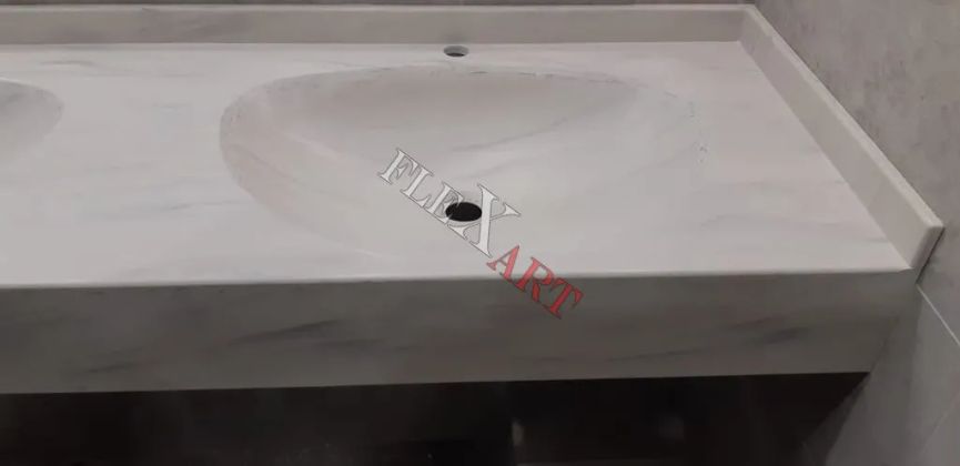 Столешница с двумя встроенными раковинами из камня под мрамор. Один край столешницы около входа в ванную комнату закруглен.