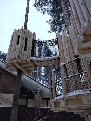 Детская крепость на деревьях из вертикально поставленного бревна является частью детского игрового комплекса на частном участке. В комплекс входят песочница-ров, мост Леонардо Да Винчи, конструктор из бревен, лазелка из вертикальных бревен с катальной горкой