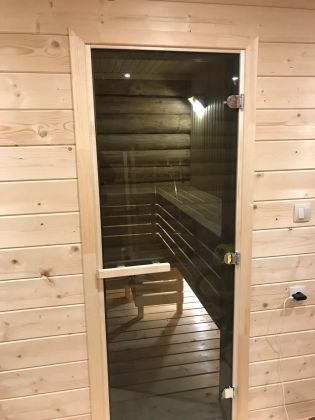 мастер устанавливает стеклянную дверь в бане